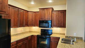 Kitchen featuring black appliances, light stone counters, and sink