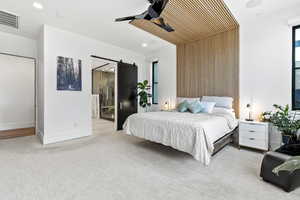 Carpeted bedroom featuring ceiling fan, a barn door, wooden walls, and ensuite bath