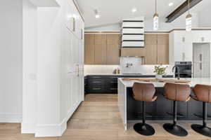 Kitchen featuring a center island, vaulted ceiling with beams, light hardwood / wood-style floors, white cabinetry, and hanging light fixtures