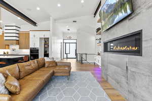 Living room featuring a tiled fireplace, wood-type flooring, and vaulted ceiling with beams