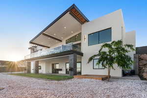 Back house at dusk featuring a balcony and a patio area