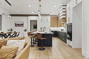 Kitchen featuring tasteful backsplash, light hardwood / wood-style floors, decorative light fixtures, a center island with sink, and white cabinets