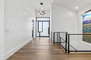 Corridor featuring lofted ceiling, hardwood / wood-style flooring, and a notable chandelier