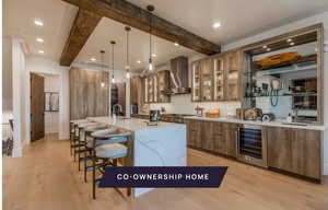 Kitchen with a spacious island, hanging light fixtures, wine cooler, wall chimney exhaust hood, and beam ceiling