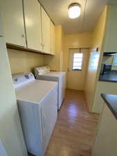 Washroom with washing machine and clothes dryer, light hardwood / wood-style flooring, and cabinets