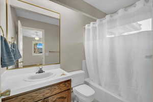 Full bathroom with ceiling fan, toilet, shower / bathtub combination with curtain, and vanity