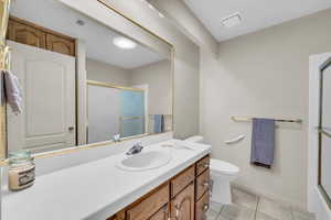 Bathroom featuring tile patterned flooring, vanity, toilet, and a shower with door