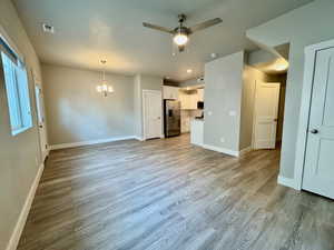 Unfurnished living room featuring light wood-type flooring and ceiling fan with notable chandelier