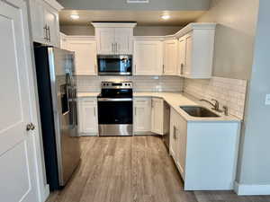 Kitchen with white cabinets, sink, appliances with stainless steel finishes, and tasteful backsplash