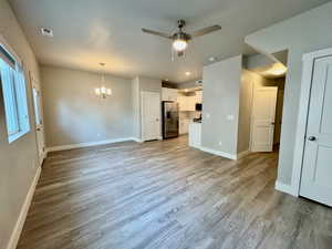 Unfurnished living room featuring ceiling fan with notable chandelier and light hardwood / wood-style flooring