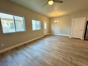 Unfurnished room featuring ceiling fan with notable chandelier and light hardwood / wood-style flooring