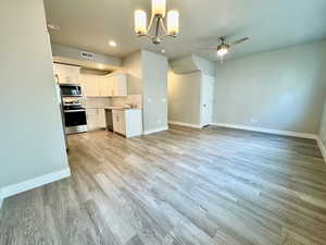 Kitchen with white cabinetry, stainless steel appliances, tasteful backsplash, light hardwood / wood-style floors, and ceiling fan with notable chandelier