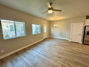 Spare room with ceiling fan with notable chandelier, a textured ceiling, and light wood-type flooring