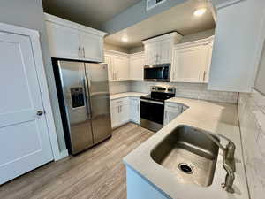 Kitchen with appliances with stainless steel finishes, light wood-type flooring, tasteful backsplash, sink, and white cabinetry