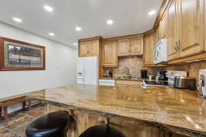 Kitchen with kitchen peninsula, white appliances, sink, dark stone countertops, and a breakfast bar area