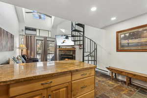 Kitchen featuring a tile fireplace, light stone counters, ceiling fan, and a baseboard heating unit