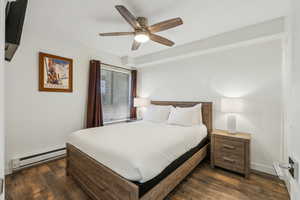 Bedroom featuring dark wood-type flooring, ceiling fan, and a baseboard heating unit