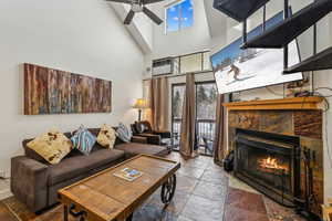 Living room featuring a tiled fireplace, ceiling fan, a healthy amount of sunlight, and a high ceiling