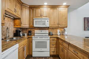 Kitchen featuring decorative backsplash, white appliances, sink, and kitchen peninsula