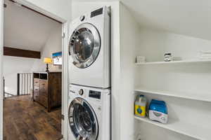 Washroom with dark hardwood / wood-style floors and stacked washer and dryer