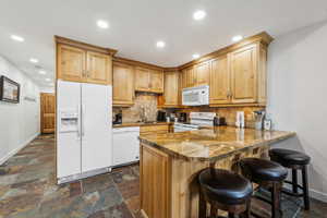 Kitchen with kitchen peninsula, backsplash, light stone counters, white appliances, and sink