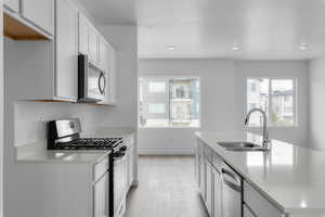 Kitchen with light wood-type flooring, a textured ceiling, stainless steel appliances, sink, and white cabinets