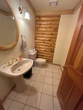 Bathroom with tile patterned flooring, toilet, ornamental molding, rustic walls, and a textured ceiling