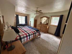 Carpeted bedroom with ceiling fan, wood walls, and a textured ceiling