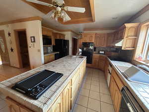 Kitchen featuring backsplash, a raised ceiling, sink, black appliances, and tile counters