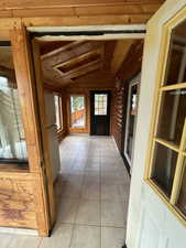 Corridor featuring wooden walls, light tile patterned flooring, wood ceiling, and lofted ceiling