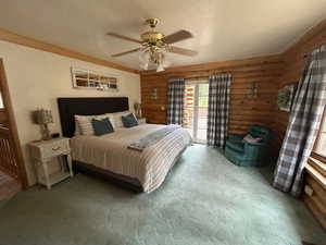 Carpeted bedroom featuring ceiling fan, rustic walls, and access to outside