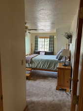 Carpeted bedroom featuring ceiling fan and a textured ceiling