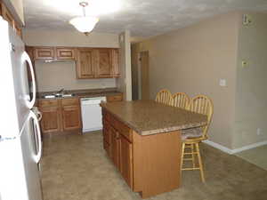 Kitchen with white appliances, sink, a kitchen island, hanging light fixtures, and a breakfast bar area