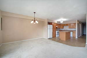 Kitchen with hanging light fixtures, a center island, a notable chandelier, light carpet, and white appliances