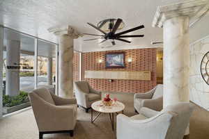 Living room with ceiling fan, carpet floors, decorative columns, and a textured ceiling