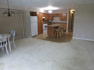 Kitchen featuring pendant lighting, stove, an inviting chandelier, a kitchen island, and white fridge