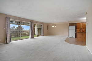 Unfurnished living room with light carpet and an inviting chandelier