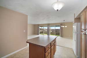 Kitchen featuring a center island, a chandelier, hanging light fixtures, light tile patterned floors, and white refrigerator