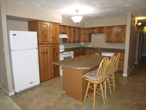 Kitchen featuring sink, pendant lighting, white appliances, a breakfast bar area, and a kitchen island