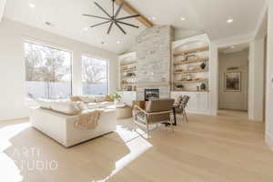 Living room featuring ceiling fan, lofted ceiling with beams, built in features, light hardwood / wood-style flooring, and a stone fireplace