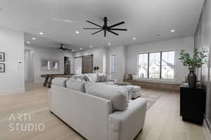 Living room with a barn door, ceiling fan, and light hardwood / wood-style flooring