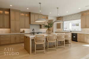 Kitchen featuring decorative backsplash, a kitchen bar, a kitchen island with sink, light hardwood / wood-style flooring, and hanging light fixtures