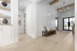 Corridor featuring beamed ceiling, french doors, light hardwood / wood-style flooring, and an inviting chandelier