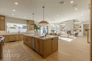 Kitchen featuring sink, a healthy amount of sunlight, decorative light fixtures, a fireplace, and a center island with sink