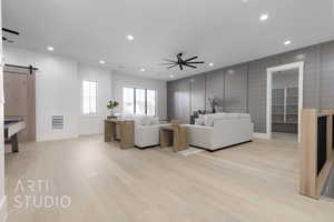 Living room with a barn door, light hardwood / wood-style flooring, and ceiling fan