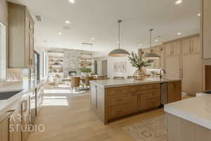 Kitchen featuring light brown cabinets, a spacious island, hanging light fixtures, light hardwood / wood-style flooring, and a fireplace