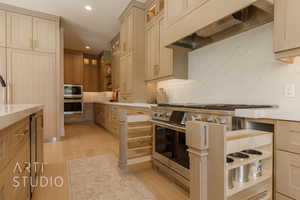 Kitchen featuring appliances with stainless steel finishes, light wood-type flooring, premium range hood, and light brown cabinetry