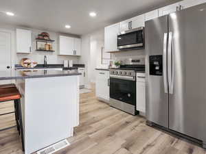 Kitchen with white cabinetry, a center island, stainless steel appliances, a breakfast bar area, and light wood-type flooring