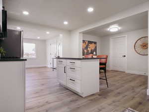 Kitchen featuring stainless steel refrigerator, a center island, a kitchen breakfast bar, white cabinets, and light wood-type flooring