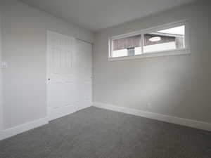 Unfurnished bedroom with multiple windows, dark colored carpet, and a closet